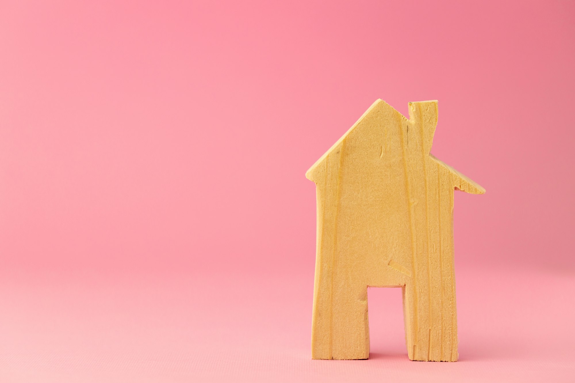 Wooden house miniature on pink background close up